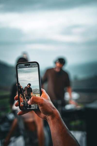 Una mano graba con el celular al DJ en la consola, con las montañas detrás.