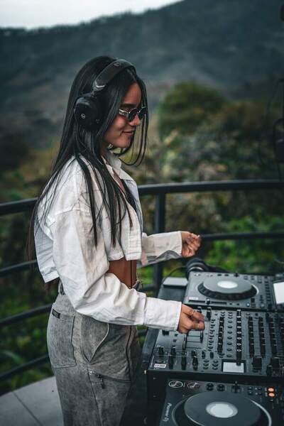 La DJ de NATMA mezcla con audífonos, con montañas verdes detrás.